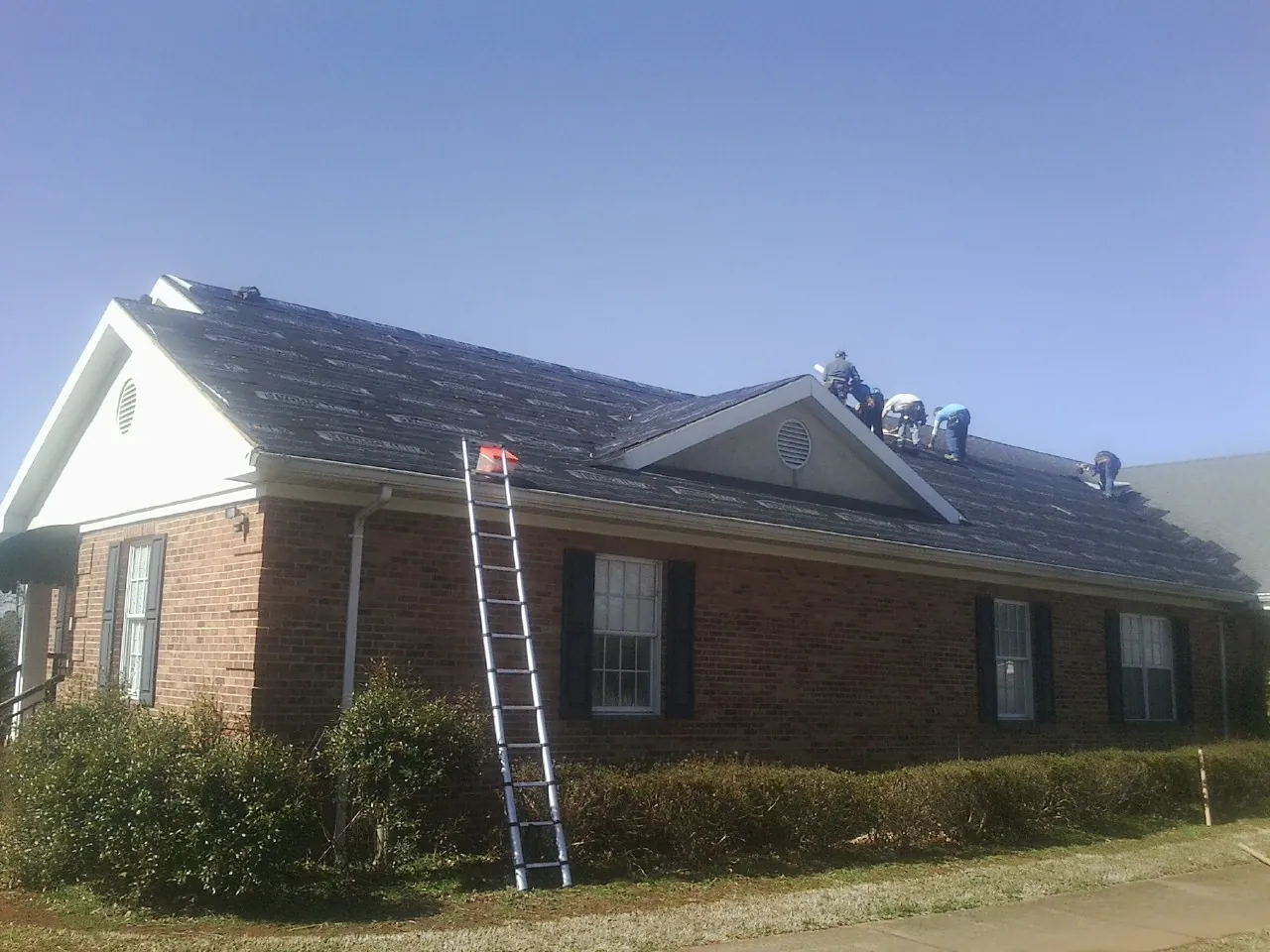 Crew tearing shingles off a brick ranch roof with a ladder set — Emergency Roof Repair work by our crew in Glengary