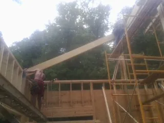 Carpenter raising a rafter beam on a new second story frame in Glengary