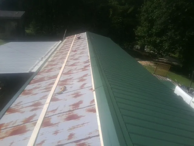 Old rusted panels beside newly installed green metal roofing — Wind Damage Roof Repair by Roofing Brothers in Glengary