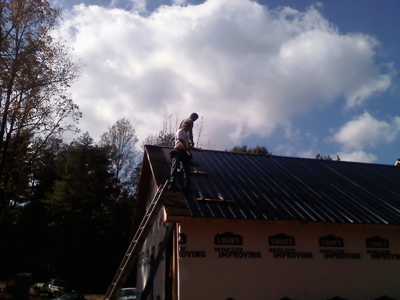 Roofer fastening dark metal panels high against a cloudy sky, from a Roof Inspection job in Glengary