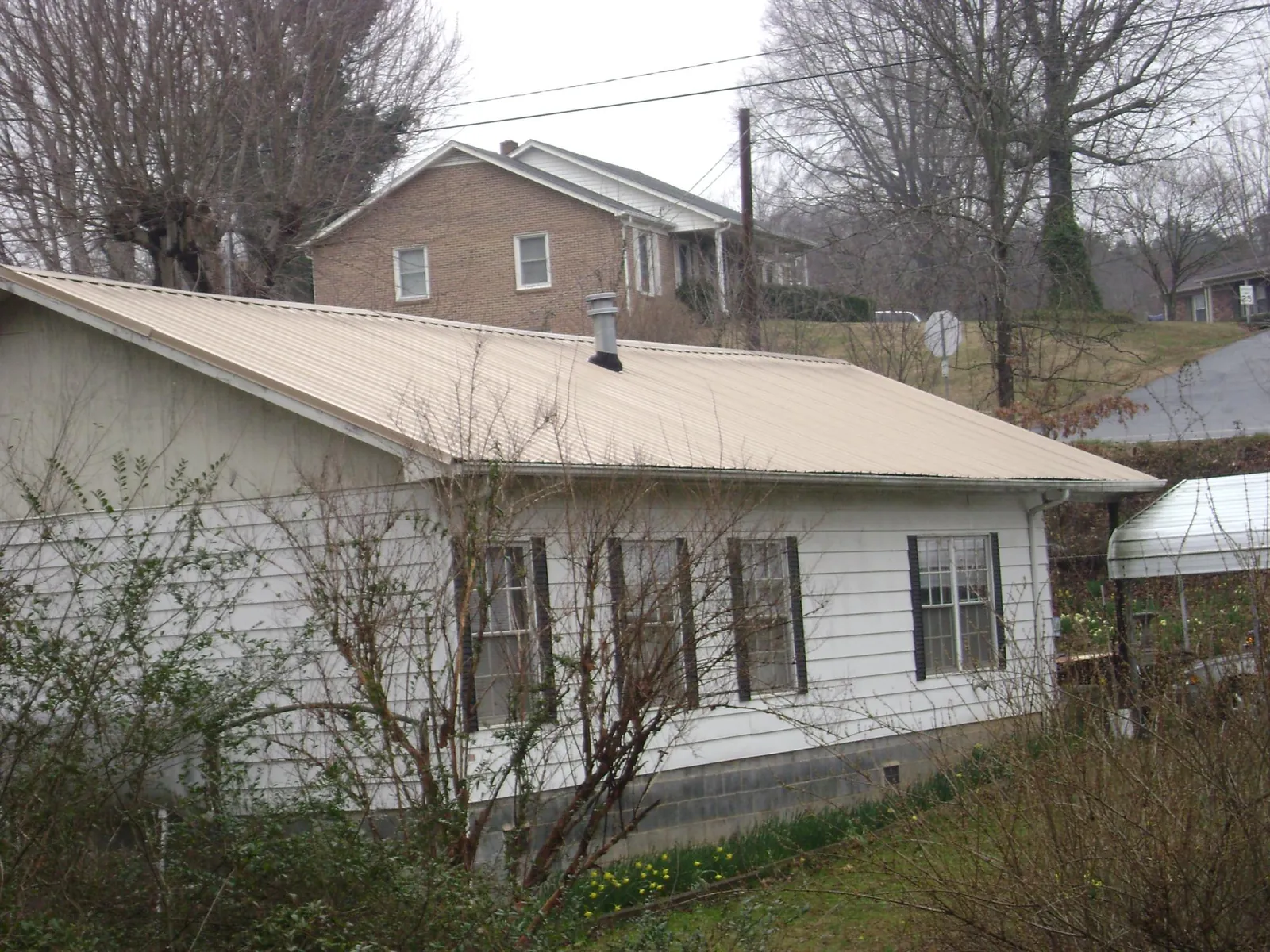 Tan metal roof on a white sided house set into a hillside — Commercial Roofing by Roofing Brothers in Glengary